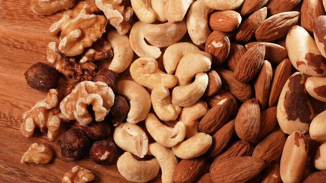 Nuts, cashews, almonds and Brazilian nuts from above. Mix with different types of nuts on a wooden plate. Close up healthy food with proteins, 4k video.