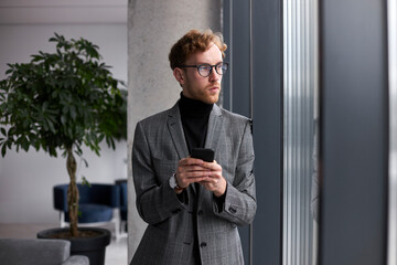 Caucasian young businessman trying new mobile applications, distant chatting, in the office interior