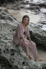 Portrait of beautiful young woman in beige silk outfit on wild rocky beach