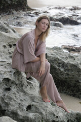 Portrait of beautiful young woman in beige silk outfit on wild rocky beach