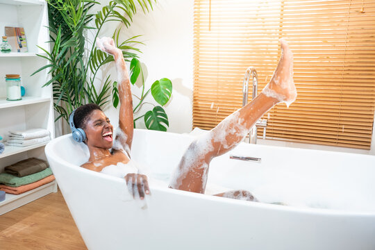 Excited woman wearing headphones happy dancing in foam bath in a sunny morning routine. Happiness and wellbeing concept. High quality photo