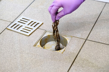 Water drain hole is clogged with hair clump. Woman hand in gloves is cleaning the bathroom sewer...