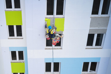 An industrial climber paints the facade of a multi-story building with colorful facade paints. Drone photography.