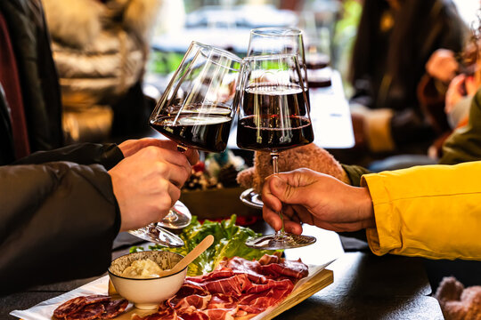 Group of friends clinking red wine glasses at pub terrace-Young people enjoying time together at winery bar with appetizers-Close up of food and alcohol drink- Celebration Holiday friendship concept 