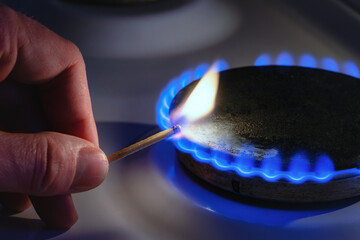 A man lights a gas stove with a match. The gas stove is lit by a match, close-up. - obrazy, fototapety, plakaty