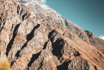 Stone rock against the background of clouds with snow on top in Altai on a bright day with trees in autumn.