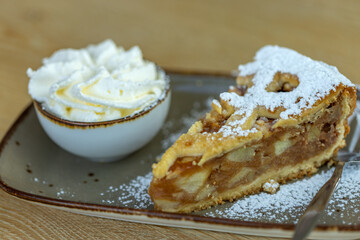 A piece of apple pie on white plate served with whipping cream on the side