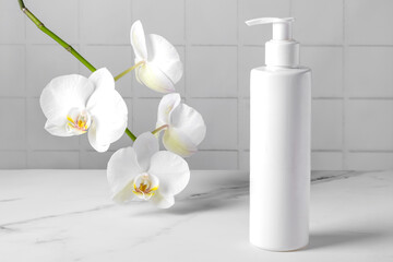 A bottle with a cosmetic product for body skin care against the background of a blooming orchid. Selective focus.