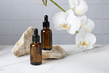 Bottles with a pipette with a cosmetic product for body skin care on a stone against a background of a blooming orchid. Selective focus.