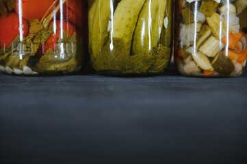 Glass jars with pickled cucumbers (pickles), pickled tomatoes and cabbage. Jars of various pickled vegetables. Canned food in a rustic composition.