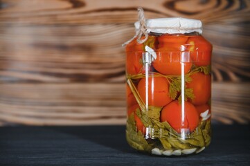 Homemade pickled tomatoes in glass jars on rustic wooden background. Fermented tomatoes in transparent glass. Homemade canned tomatoes.