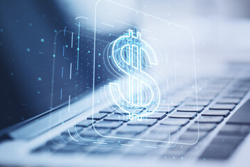 Close up of laptop computer on desktop with glowing dollar sign hologram on blurry background. Concept for investment and passive income, currency growth. Double exposure.
