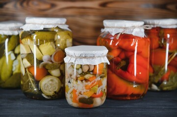 Canned cucumbers and tomatoes with craft lids on a wooden background. Cucumbers and tomatoes with place for text. Stocks of canned food. Harvest, stocks for the winter.