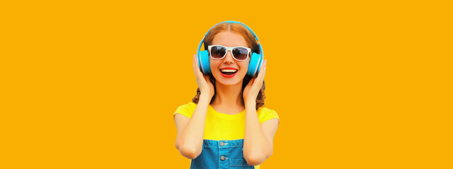 Portrait of happy smiling young woman with headphones listening to music on yellow background