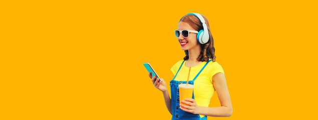 Portrait of smiling young woman in headphones listening to music with smartphone and drinking juice...