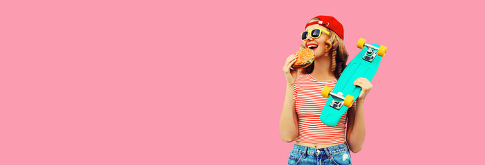 Portrait of stylish young woman with burger fast food and skateboard wearing baseball cap,...