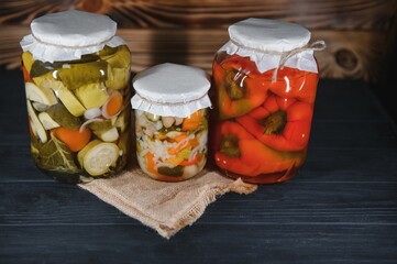 Glass jars with pickled cucumbers (pickles), pickled tomatoes and cabbage. Jars of various pickled vegetables. Canned food in a rustic composition.
