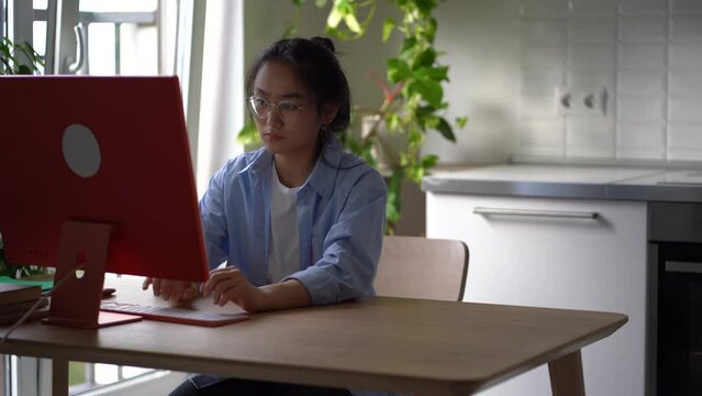 Tired nervous Asian business woman sits at computer at home office after finishing typing takes off glasses. Young casual Chinese girl remote worker stops working leans back in chair with relief 