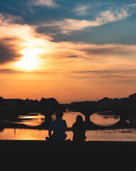 Pareja mirando el atardecer desde un puente en florencia, italia