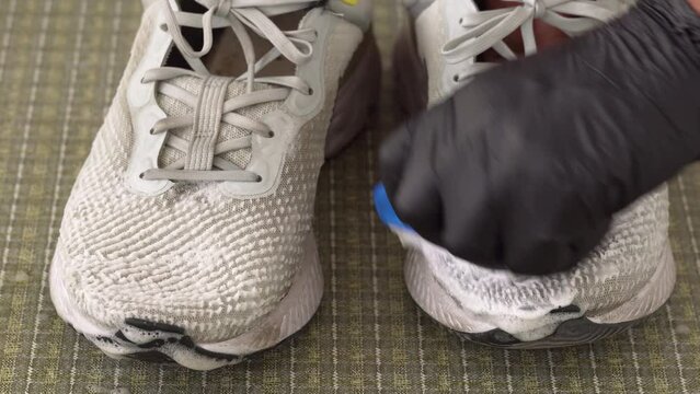 Cleaning sneakers with brush and soap close up. Hand wearing black rubber glove cleaning dirty sneakers with a brush and soap foam. 4K resolution video.