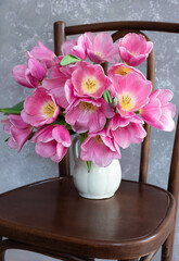 pink tulips in a ceramic jug on a wooden chair