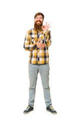 Young adult redhead man with a long beard standing full body isolated winks an eye and holds an okay gesture with hand.