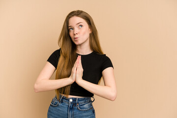 Young redhead woman cut out isolated holding hands in pray near mouth, feels confident.