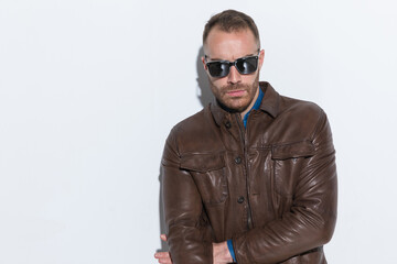 cool fashion guy in brown leather jacket with sunglasses posing