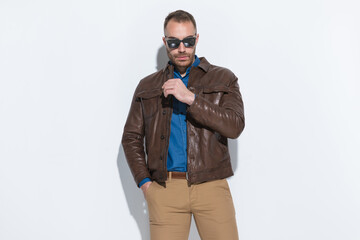 Fototapeta premium cool bearded guy wearing brown leather jacket and posing with hands in pockets