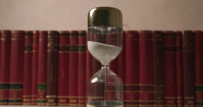 clepsydra in front of row on books in a library, time is passing by fast when you are studying for exams 