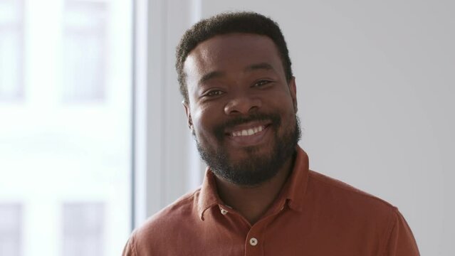 Close up portrait of young handsome african american man smiling to camera, standing at home, tracking shot, slow motion