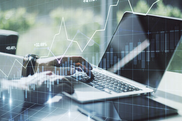 Abstract creative financial graph with hand typing on laptop on background, financial and trading concept. Multiexposure