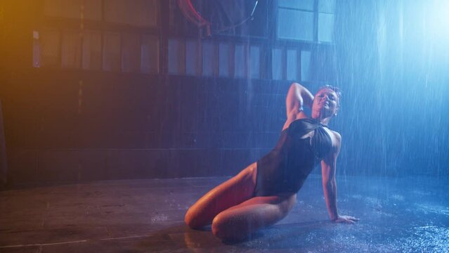 Woman dancing on wet floor under pouring water rain, performing sexy moves by fit wet body. Sensual adult woman shows wide opened stretched legs 4K. Erotic performance in privat room of strip club