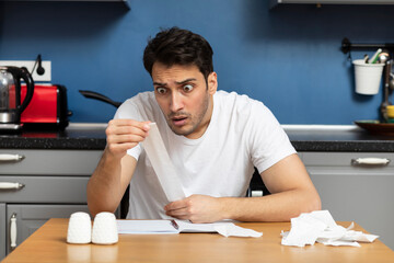 Close up of unhappy man sitting at the table, stressed and confused by calculate expense from...