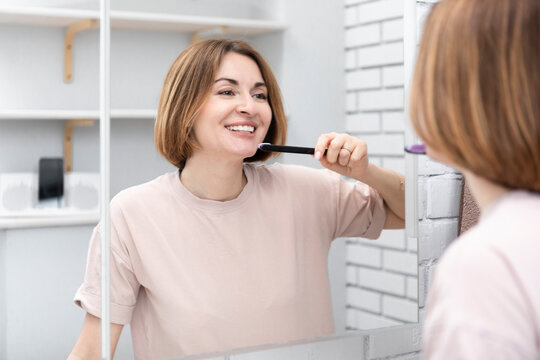 Attractive woman brushing teeth and looking at the mirror in the bathroom	
