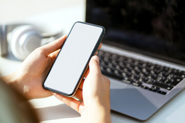 Cropped view of the woman holding smartphone with blank screen, messaging in social media while sitting at the street cafe. Female chatting, reading text message, online shopping. Mockup