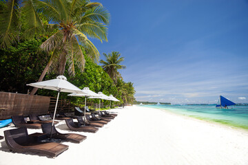 Sun umbrellas and beach chairs on tropical beach with palm trees
