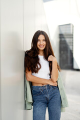 Portrait of smiling woman with beautiful long hair wearing jeans, tank top looking at camera on urban street. Happy fashion model posing for pictures outdoors. Natural beauty  