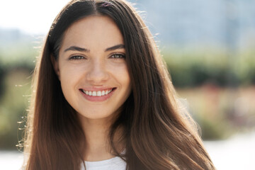 Closeup Portrait of gorgeous smiling woman with beautiful eyes and long hair looking at camera on the street. Happy fashion model posing for pictures outdoors. Natural beauty concept 