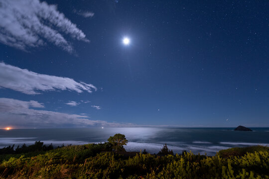 Moon shines brightly over the Pacific Ocean on a starry night at the Oregon Coast