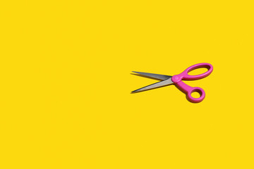 Pair of bright pink scissors on a yellow background