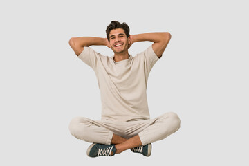Young caucasian man sitting on the floor isolated on white background stretching arms, relaxed position.