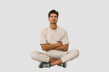 Young caucasian man sitting on the floor isolated on white background tired of a repetitive task.