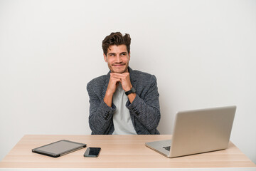 Young entrepreneur man working with a laptop isolated keeps hands under chin, is looking happily aside.