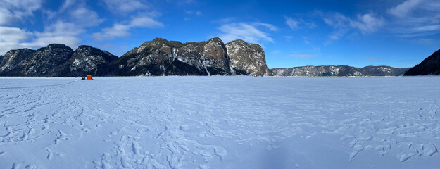 Ice fishing huts with cliffs in the background on a clear blue winter day, Eternity Bay, Saguenay Fjord, Cabada.