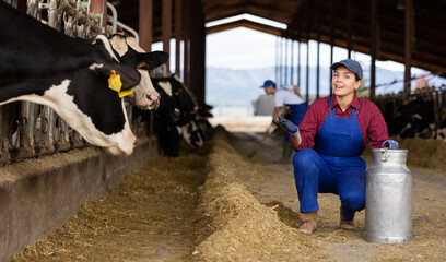 Smiling farmer woman stands in open cowshed and shows cow farm
