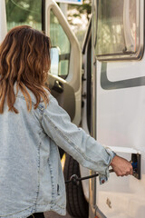 Fototapeta na wymiar middle-aged woman with long hair and denim shirt, filling motorhome water tank at a camper service area,