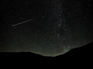 Shooting stars cross the night sky above the mountains