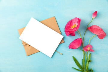 Fototapeta premium Blank greeting card with pink poppy flowers bouquet on pastel blue background. Wedding invitation. Mock up