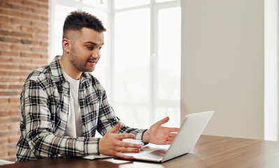 A happy young man works at a computer and communicates online.